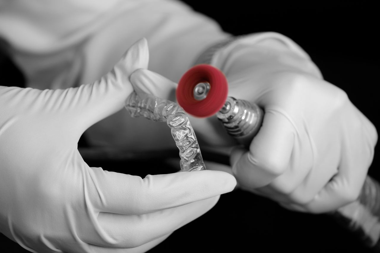 A dental technician uses a grinder to polish a clear aligner in a laboratory setting.